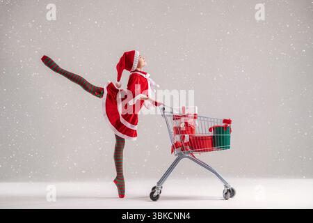 Ballerina im Weihnachtsmannkostüm tanzt mit einem Einkaufswagen voller Geschenke Stockfoto