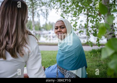 Eine Frau in einem blaugrünen Hijab und einer Bluse ist draußen unter Laubbäumen Stockfoto