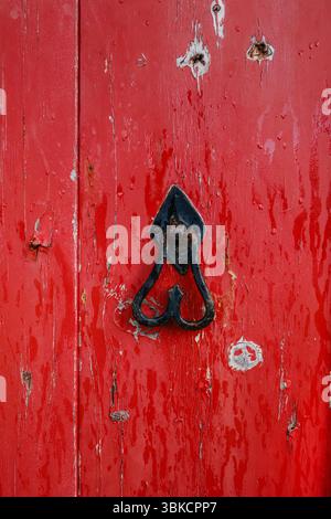 Rote Holztür mit einem einzigartigen herzförmigen Metallklopfer. Vintage-Eingang, verwittertes Holz, charmantes Detail, alte Architektur, Wohnkultur Stockfoto