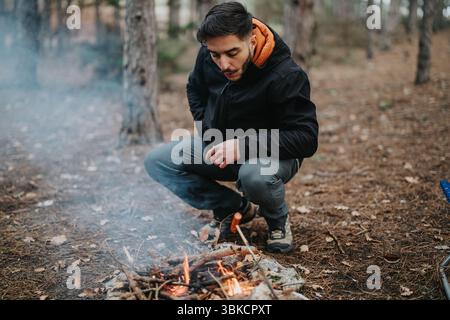 Ein Mann, der ein kleines Feuer in einem bewaldeten Gebiet während eines ruhigen Outdoor-Abenteuers pflegt Stockfoto