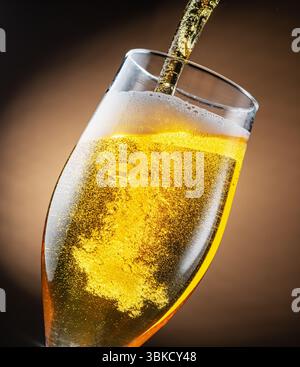 Helles Bier auf braunem Hintergrund in das Bierglas gießen. Helle Bläschen im mit Bierstrom gebildeten. Stockfoto