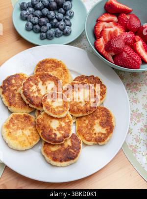 Syrniki oder gebratene Hüttenkäsepfannkuchen auf weißem Teller auf dem Tisch. Stockfoto
