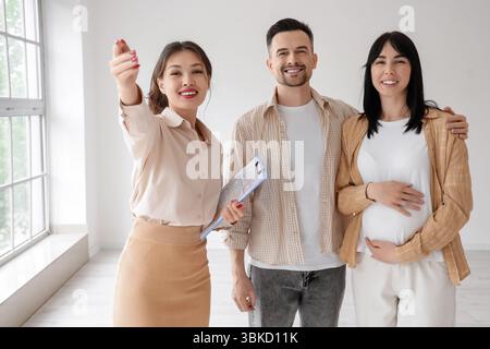 Weibliche asiatische Immobilienmaklerin zeigt schwangeren Paaren neues Haus Stockfoto