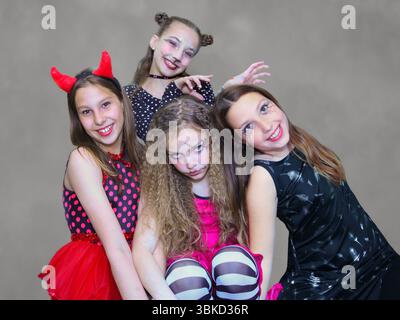 Vier junge Mädchen in farbenfrohen Halloween-Kostümen posieren drinnen, lächeln und blicken in die Kamera. Stockfoto