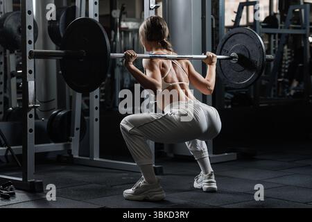 Fitte Frau, die Langhantelhocken in einem modernen Fitnessstudio macht, demonstriert Kraft, Konzentration und Kraft beim funktionellen Workout-Training. Stockfoto
