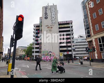 Fußgänger überqueren die Straße vor dem mit Graffiti bedeckten NCP-Parkplatz an der Great Eastern Street, London, Großbritannien, ein ikonisches Beispiel für brutalistische Architektur, die sich mit East Londons lebendiger Street Art-Kultur kreuzt Stockfoto