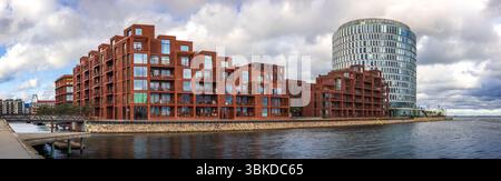 Moderne Hafenarchitektur im Kopenhagener Stadtteil Nordhavn mit roten Backsteingebäuden und einem markanten Glasbüroturm Stockfoto
