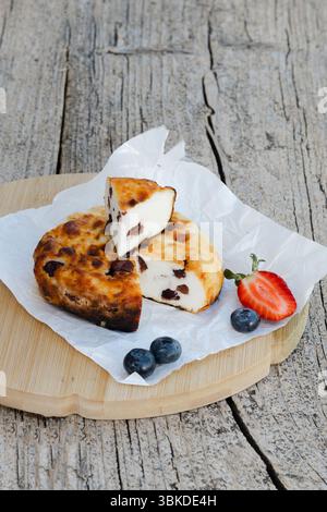 Runder Hüttenkäseauflauf mit Rosinen, Heidelbeeren und Erdbeeren auf Backpapier und Holzbrett, ein gesundes und köstliches Frühstück Stockfoto