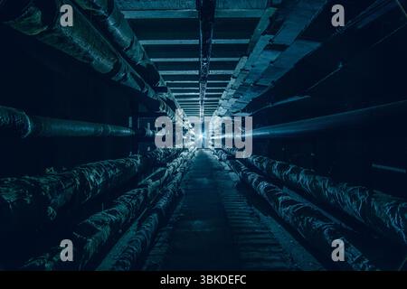 Dunkler unterirdischer Beton-Kommunikationstunnel mit Rohren und Drähten in kalten Farben. Stockfoto