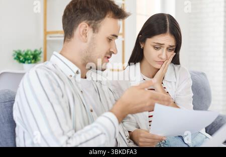 Verärgertes junges Paar, das auf dem Sofa sitzt und zu Hause Finanzdokumente durchsucht Stockfoto