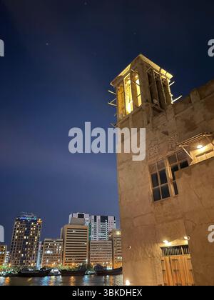 Nachtansicht auf die traditionellen Emirati-Häuser von Al Seef auf der rechten Seite und die modernen Bur Dubai-Gebäude auf der linken Seite entlang des malerischen Dubai Creek. Stockfoto