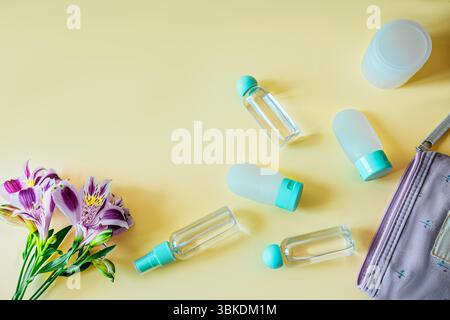 Flache Komposition von Reisetoilettenflaschen, Kosmetikbeutel und frischen Blumen auf pastellfarbenem Hintergrund. Helle, saubere und feminine Reiseutensilien Stockfoto
