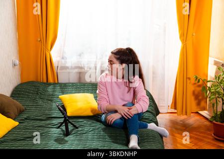 Leidenschaftliche Frau, die auf einem Bett sitzt und ein aufschlussreiches Social-Media-Video für ihre Follower aufnimmt. Weitsicht. Stockfoto