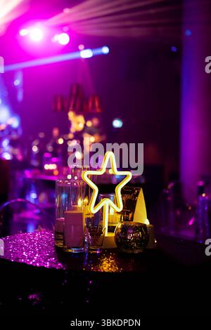 Ein Tischaufsatz mit einem leuchtenden Neonstern, Kerzen und einer Pailletten-Tischdecke, in hellem lila Licht getaucht. Stockfoto