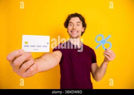 Junger Mann, der eine Kreditkarte und ein Prozentsymbol auf gelbem Hintergrund hält, das ein Finanzangebot zeigt Stockfoto