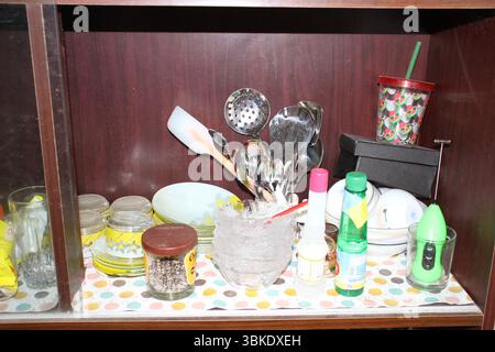 Das Innere eines hölzernen Küchenschranks mit einer Vielzahl von Küchenartikeln, die auf einem farbenfrohen Polka-Dot-Regalauskleider angeordnet sind. Links ist eine Brille. Stockfoto