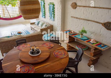 Charmantes Inneres eines Ferienhauses an der Küste mit einem hölzernen Esstisch, lebhaftem Dekor und komfortablem Sitzbereich in Rincon del Mar. Stockfoto