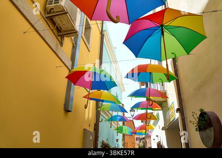 Olbia, Sardinien, Italien - 14. Juni 2025: Bunte Regenschirme schmücken eine enge Gasse in Olbia auf Sardinien und sorgen für sommerliche Farbenpracht *** Bunte Regenschirme schmücken eine enge Gasse in Olbia auf Sardinien und sorgen für sommerliche Farbenpracht Stockfoto