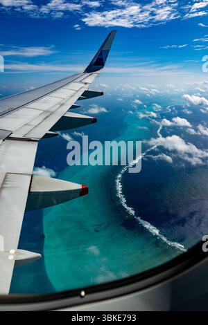 Ein Luftbild aus einem Flugzeugfenster zeigt den Flügel des Flugzeugs über einem tropischen Ozean mit einem Korallenriff. Stockfoto