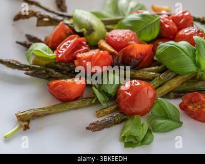 Eine lebendige Mischung aus gegrilltem Spargel und Tomaten, garniert mit Basilikum, perfekt für eine leichte und nahrhafte vegetarische Mahlzeit. Stockfoto