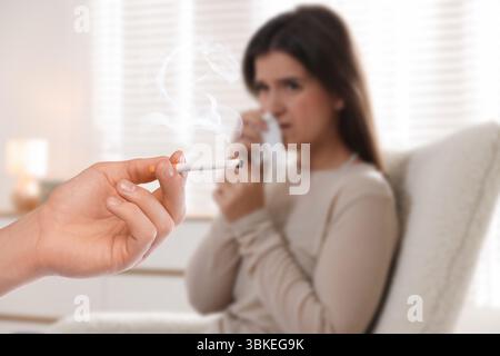 Passivrauchen. Frau, die ihre Nase mit Taschentuch bedeckt, weil ein Mann in der Nähe raucht. Selektiver Fokus Stockfoto