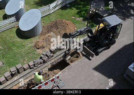 Bagger und Bauarbeiter graben Graben auf dem städtischen Bürgersteig. Städtische Baustelle vom Fenster „Apartment“ aus gesehen Stockfoto