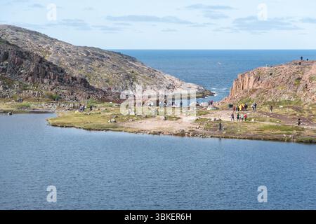Teriberka, Russland - 13. Juni 2025: Touristen erkunden die felsige Küstenlandschaft mit Klippen, Felsbrocken und arktischer Vegetation in der Nähe der Barentssee Stockfoto