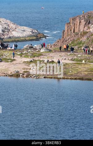 Teriberka, Russland - 13. Juni 2025: Touristen erkunden die felsige Küstenlandschaft mit Klippen, Felsbrocken und arktischer Vegetation in der Nähe der Barentssee Stockfoto