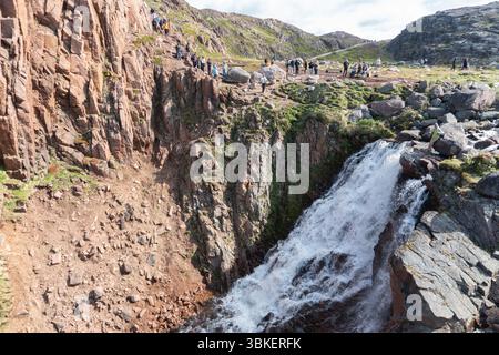 Teriberka, Russland - 13. Juni 2025: Touristen versammeln sich an einem sonnigen Tag um den Batarayskiy-Wasserfall in Teriberka, umgeben von schroffen arktischen Felsen Stockfoto