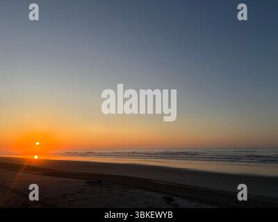 Goldene Sonne taucht einen ruhigen Strand und ruhige Meereswellen in einen wunderschönen Sonnenaufgang. Eine ruhige, friedliche Küstenlandschaft Stockfoto
