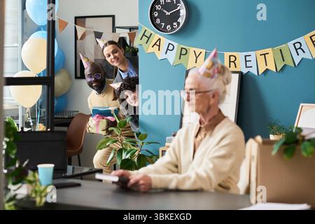 Ein hochrangiger kaukasischer Mann sitzt am Schreibtisch, während ihn verschiedene Kollegen überraschen Stockfoto
