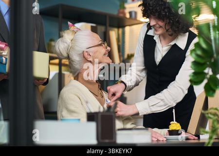 Ältere kaukasische Frau lächelt, während sie ein Geburtstagsgeschenk von einem jungen Erwachsenen erhält Stockfoto