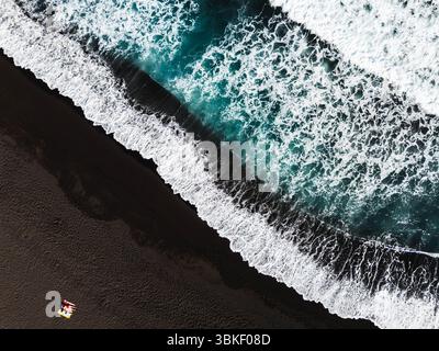 Impressive top down shot of the deep blue ocean with beautiful caucasian woman lay down at the black sand beach, Tenerife, Canary Islands, Spain Stockfoto