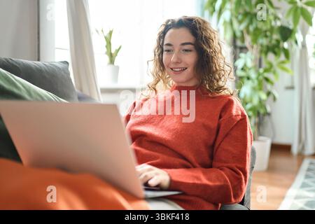 Entspannte, glückliche junge Frau, die beim Surfen zu Hause mit dem Laptop auf dem Sofa saß. Stockfoto