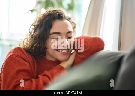 Junge glückliche, traumhafte Frau, die sich zu Hause mit geschlossenen Augen auf der Couch entspannt. Stockfoto