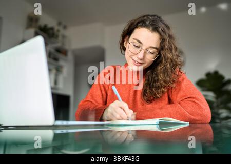 Junge Studentin mit Laptop, die sich zu Hause ein Online-Webinar angeschaut hat. Stockfoto