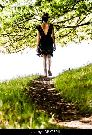 Eine Frau in einem schwarzen Kleid läuft barfuß auf einem Weg durch ein grasbewachsenes Gebiet. Stockfoto