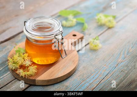 Lindenhonig im Glas mit hölzernem Honiglöffel und Lindenblüte auf hölzernem Hintergrund Stockfoto