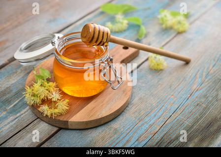 Lindenhonig im Glas mit hölzernem Honiglöffel und Lindenblüte auf hölzernem Hintergrund Stockfoto