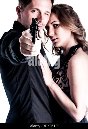Ein Mann zeigt mit einer Waffe direkt auf den Zuschauer, während eine Frau ihn von hinten umschließt. Der Mann trägt ein schwarzes Hemd und die Frau trägt ein Stockfoto