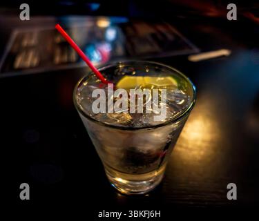 Ein klassischer Gin und Tonic, serviert auf Eis in einem kurzen Glas, garniert mit einem Limettenkeil und gerührt mit rotem Strohhalm. Frisch, erfrischend und perfekt für Stockfoto