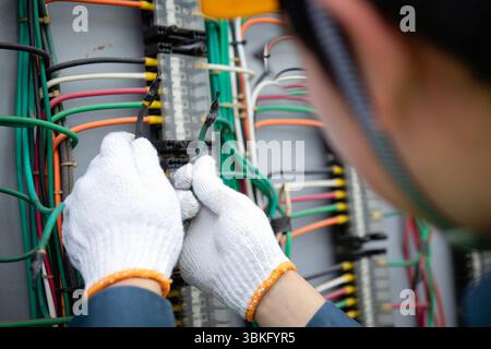 Ein Kraftwerksingenieur, der mit Elektrodrähten arbeitet, weiße Handschuhe und Schutzhelm trägt und sich auf die Reparatur und Wartung des Systems mit ColorFu konzentriert Stockfoto