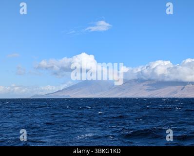 Ein schwacher Regenbogen erscheint über den Bergen von Maui, vom Meer aus gesehen an einem klaren Tag. Stockfoto