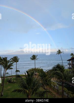 Regenbogenbögen über dem Pazifik und Palmen an der Küste von Maui, Hawaii, mit Blick auf ferne Inseln. Stockfoto