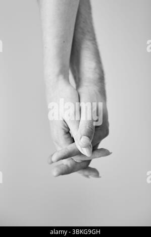 Zwei Hände in der Hand vor neutralem Hintergrund gehalten. Nahaufnahme der Hand von Mann und Frau. Konzept von Intimität, Unterstützung und Vertrauen. Schwarzweißbild. Stockfoto