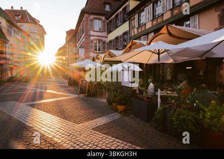 Ribeauvillé, Elsass, Frankreich: Gäste auf der Terrasse der Brasserie La Post in der mittelalterlichen Gasse mit Fachwerkhäusern, die vom Sonnenuntergang beleuchtet werden Stockfoto