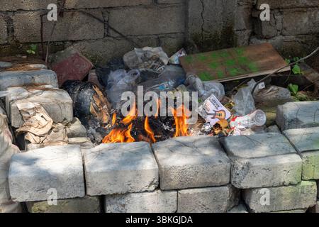 Gili, Lombok, Indonesien - 8. Januar 2025: Müllhaufen brennt vor einer Ziegelmauer. Das Feuer ist klein und der Müll ist verstreut Stockfoto