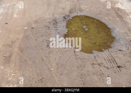 Wasserpfütze auf einer unbefestigten Straße. Das Wasser ist grün und hat ein schlammiges Aussehen Stockfoto