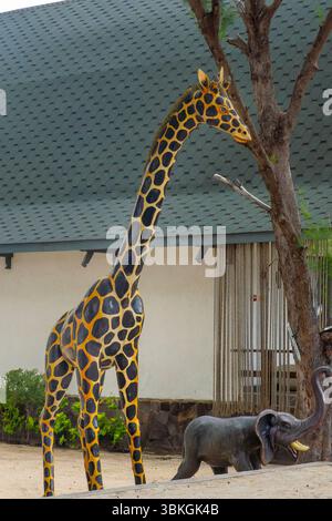 Gili, Lombok, Indonesien - 8. Januar 2025: Giraffen-Statue steht vor einem Gebäude. Eine kleine Elefantenstatue läuft dahinter Stockfoto