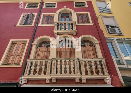 Flacher Blick auf ein Gebäude mit verzierten Balkonen, Holzläden und einer auffälligen roten Fassade in rovigo, italien Stockfoto